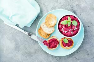 Homemade bruschetta with beetroot hummus on small toast on a plate and a table knife on the table. Top view photo