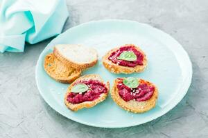 Homemade bruschetta with beetroot hummus on small baked baguette toast on a plate on the table. Close-up photo