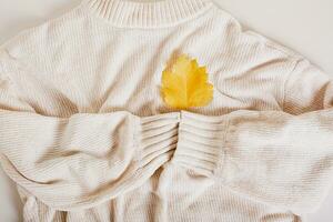 Cozy autumn sweater holds with its sleeves a yellow autumn leaf on a heart top view photo