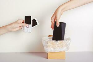 The hand throws the smartphone into the trash and the second hand holds push-button phones photo