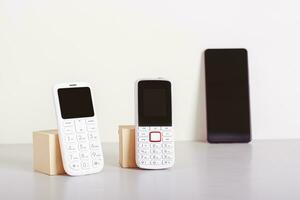 Two old-fashioned white push-button phones are on the table and a smartphone is in the background photo