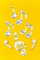 Wireless headphones and music notes cut from paper on a yellow background. Music imitation concept. Vertical view photo