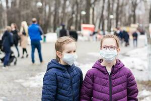 Two girls in protective face masks in the park, at a distance from the crowd of people. Walk the new normal photo