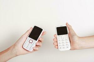 Two hands are holding push-button phones on a light background photo