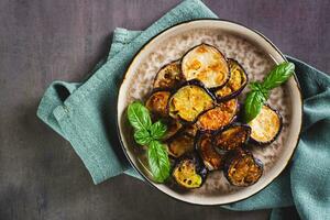 Close up of appetizing fried eggplant with spices and herbs on a plate on the table top view photo