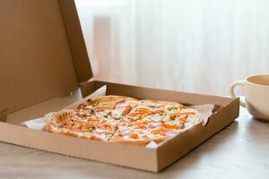 Takeaway food. Pizza in a cardboard box on the table in the kitchen. photo