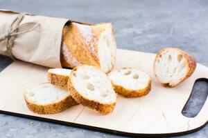 Fresh baguette in wrapping paper cut into pieces on a cutting board on a table photo