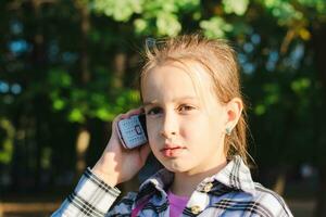 grave niña hablando en un tugurio teléfono en un verano soleado parque foto