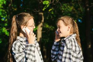 dos alegre muchachas hablando en tugurio Los telefonos en un soleado verano parque foto