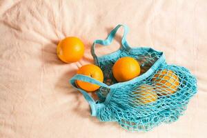 Fresh oranges in a mesh bag on a fabric background. Zero waste. Hard light photo