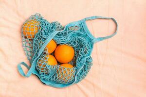 Fresco naranjas en un malla bolso en un tela antecedentes. cero residuos foto