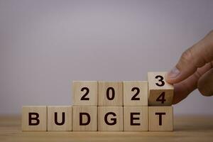 2024 Budget planning and allocation concept. Hand flips wooden cube and changes the inscription BUDGET 2023 to BUDGET 2024 with grey background on wooden table, Copy space. photo