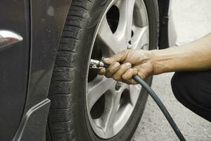 man driver hand inflating tires of vehicle, removing tire valve nitrogen cap for checking air pressure and filling air on car wheel at gas station. photo