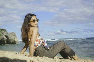 Young Asian woman sit on the beach sand. Portrait sexy Asian lady traveling and relaxing in the summer with tropical nature. photo