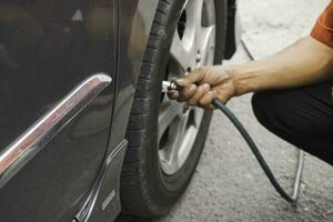 man driver hand inflating tires of vehicle, removing tire valve nitrogen cap for checking air pressure and filling air on car wheel at gas station. photo