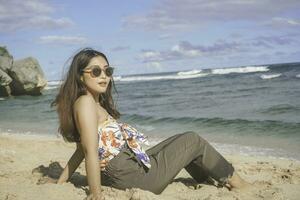 joven asiático mujer sentar en el playa arena. retrato sexy asiático dama de viaje y relajante en el verano con tropical naturaleza. foto