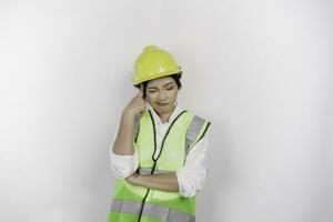 A thoughtful young woman labor worker wearing safety helmet and vest is looking aside to an idea on copy space , isolated by white background. Labor's day concept. photo