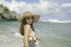 A happy young Asian woman wearing beach hat is posing to the camera at the beach in Gunungkidul, Indonesia photo