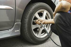 man driver hand inflating tires of vehicle, removing tire valve nitrogen cap for checking air pressure and filling air on car wheel at gas station. photo