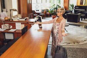 maduro mujer viene a el hotel a el recepción. ella es cansado de esperando para recepcionista. foto