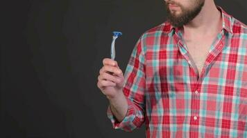 Brünette Hipster halten Rasierapparat im seine Hand isoliert auf dunkel grau Hintergrund video