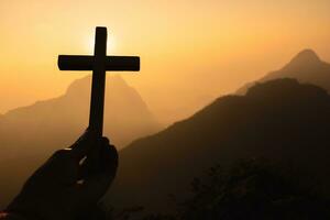 silueta de manos de mujer rezando con cruz en el fondo del amanecer de la naturaleza, crucifijo, símbolo de fe. oración de crisis de vida cristiana a dios. foto