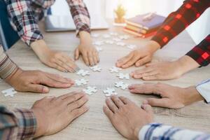 Group of business people putting their hands on a table with jigsaw puzzles. concept of cooperation teamwork Help and support in business Symbols of associations and connections business strategy. photo