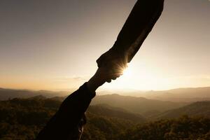 Silhouette of reaching, giving a helping hand, hope and support each other over sunset background, Help, hope and support each other over sunset background. photo