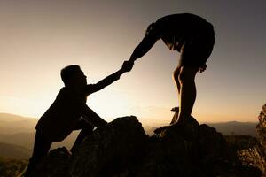 Silhouettes of two people climbing on mountain and helping. Help and assistance concept. Silhouette of  Teamwork  on the mountains Helping hand,  Sports training. photo