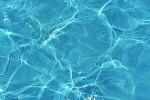 Blue water with ripples on the surface. Defocus blurred transparent blue colored clear calm water surface texture with splashes and bubbles. Water waves with shining pattern texture background. photo