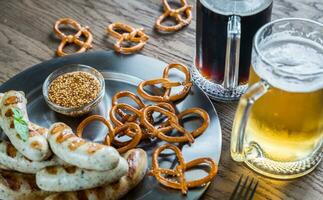 A la parrilla salchichas con pretzels y tazas de cerveza foto