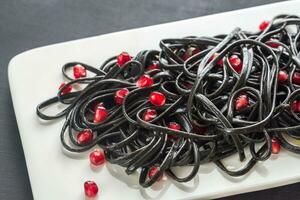 Black pasta with pomegranate seeds photo