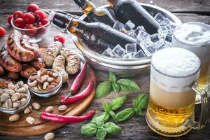 A la parrilla salchichas con aperitivos y tazas de cerveza foto