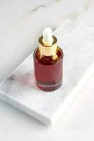 Red glass cosmetic bottle with a dropper on a marble background with podium. Natural cosmetics concept, natural essential oil and skin care products with ginseng photo