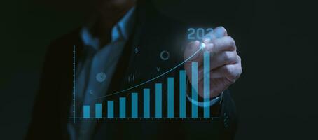 Businessman holds pen and draws up arrow graph of the company in future years 2023 to 2024. Challenge planning and business strategy, setting goals, and planning work. photo