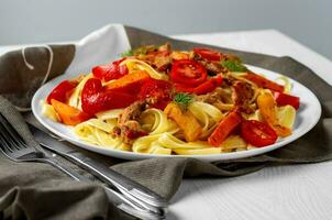 Fettuccine with fried meat, carrots, bell peppers, dill tomatoes, decorated with a cloth. Pasta with vegetables. View from above. photo