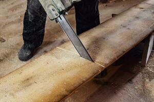 carpenter is sawing a wooden board with an electric saw. Flying splinters.  old village carpentry workshop. photo