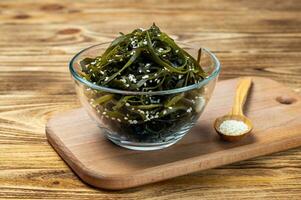 Algae Laminaria kelp in a glass bowl strewing sesame on a wooden board. Seaweed salad. Healthy food concept. photo