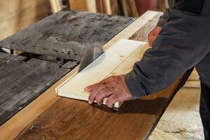 carpenter saws a wooden board with a carpentry machine.  old rustic carpentry shop. Working on woodworking machine photo