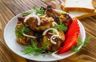 Closeup fried chicken wings, with fresh tomatoes, onions, dill, garlic and bread on a wooden background. The concept of meat food. photo