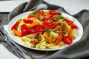 Fettuccine con frito carne, zanahorias, campana pimientos, eneldo Tomates, decorado con un paño. pasta con vegetales. lado vista. foto