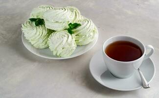 hecho a mano manzana figurado hecho en casa malvavisco con menta en un blanco plato y té en un blanco taza en un hormigón mesa. foto