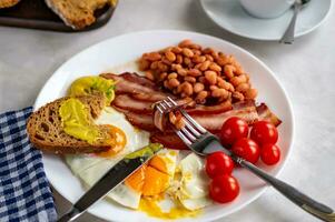 empezado con un abundante desayuno de revuelto huevos, tocino, frijoles, Cereza Tomates, hecho en casa pan, té y Malvaviscos en un hormigón encimera Inglés desayuno concepto. foto