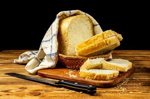 Fresh white wheat homemade bread on a wooden board on a wooden table, covered with a towel. Homemade cakes, pastries photo