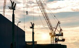 silueta construcción grua trabajando a construcción sitio en contra puesta de sol cielo. trabajador colgando en grua. construcción negocio. construcción industria. urbano desarrollo en progreso. edificio el futuro foto