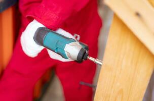Carpenter and screwdriver hand tool. A skilled worker set to work drilling and installing wooden fixtures, using electric screwdriver to construct and repair parts of house with precision and care. photo