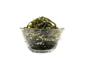 Kelp algae  in a glass bowl, sprinkled with sesame seeds, isolated on a white background. Salad. Healthy food concept. photo