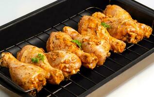 Raw chicken drumsticks marinated red with turmeric, garlic, mustard and parsley. Lined with chicken on a wire rack, ready to bake. B-B-Q. Home kitchen. Side view. photo