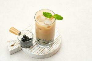 Boba milk tea with brown sugar syrup in a tall glass with ice and mint leaf photo
