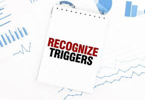 White notepad with text RECOGNIZE TRIGGERS on the financial documentation. Finance and business concept photo